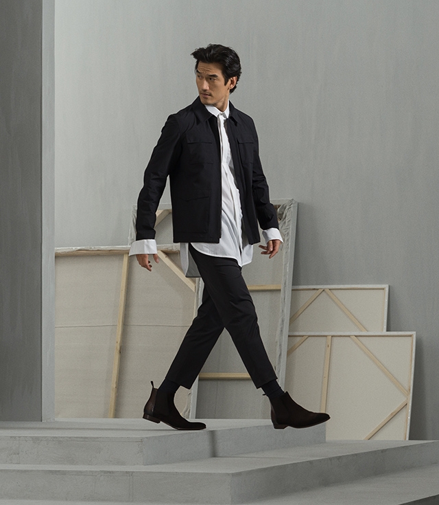 Male model descends steps in Magnanni’s Renley dress boot in brown styled with black pants, black jacket, and white oxford shirt.