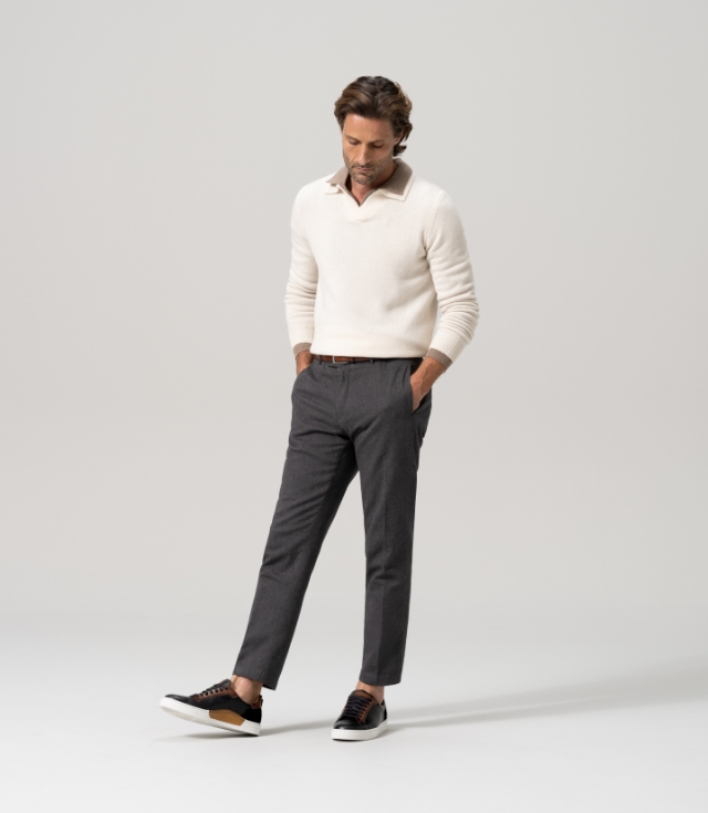 A man wears a white sweater, grey pants, and Magnanni Amadeo Black / Brown sneakers.