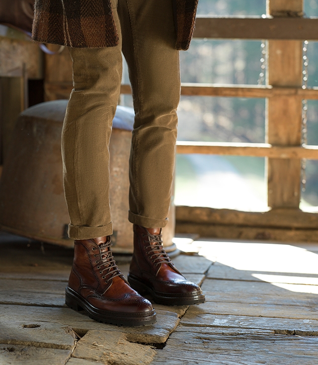 A male model stands in a cabin wearing cuffed corduroy pants and Magnanni Daroca boots in Cognac.
