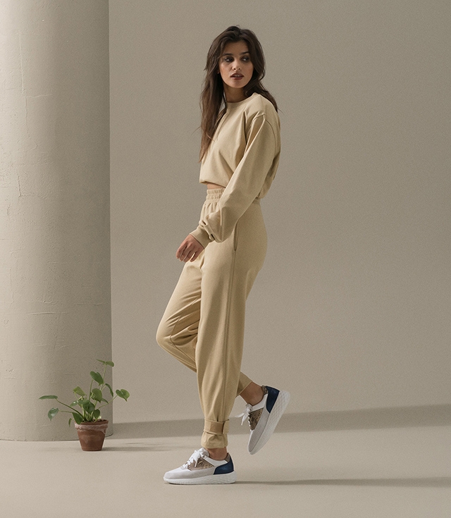 A woman steps and looks to her left while wearing tan sweats and Magnanni Ella sneakers.