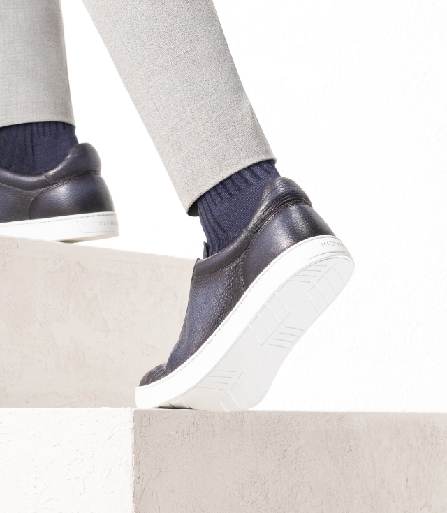 A man walks up the stairs while wearing grey pants, navy socks, and Magnanni Leve navy sneakers.