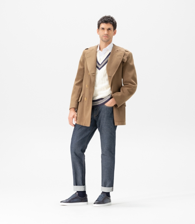A man wears a brown coat, cuffed navy jeans, and Magnanni Leve Navy sneakers.