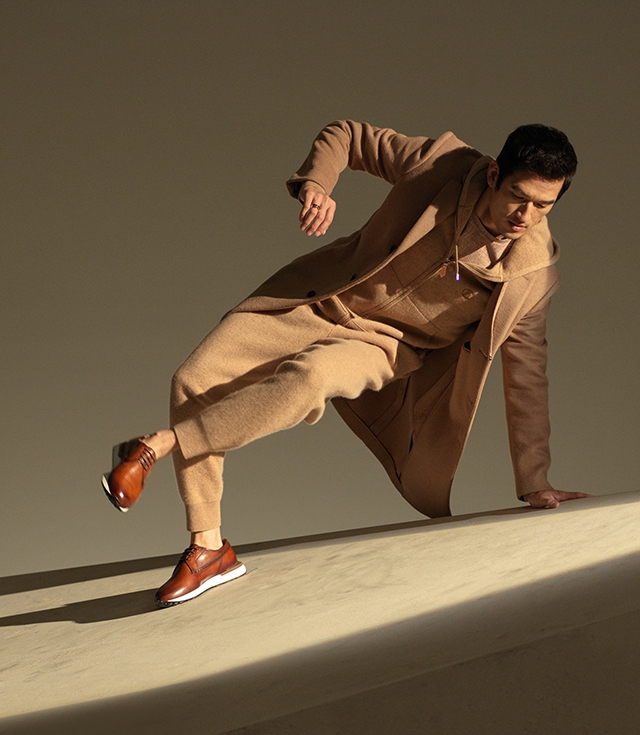 A male model wearing a casual tan outfit poses on a incline plane in Magnanni Leiva dress sneakers in Cognac.