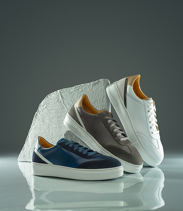 Magnanni Spero sneakers in Navy, Grey, and White sit near a rock in a very shiny room.