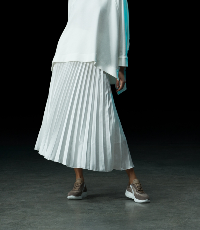 A woman stands in a dark room while wearing a white dress and Magnanni Aero Taupe sneakers.