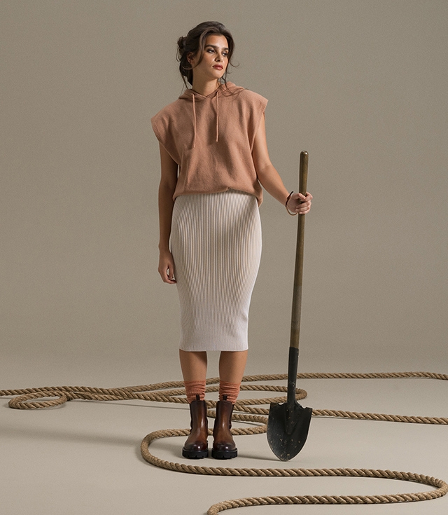 A woman holds a shovel while wearing a salmon sweatshirt, striped skirt, and Magnanni Aurora boots.
