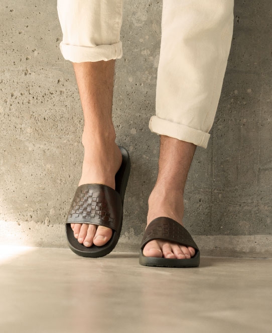 Close up of a male model wearing white pants and Magnanni Playa Woven Mid-brown slides.