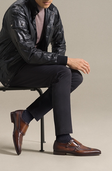 A male model sits in a metal chair wearing black pants, black jacket, and Magnanni Jones dress shoes.