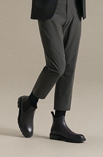 A male model steps forward in grey pants, black socks, and Magnanni Beckam boots.